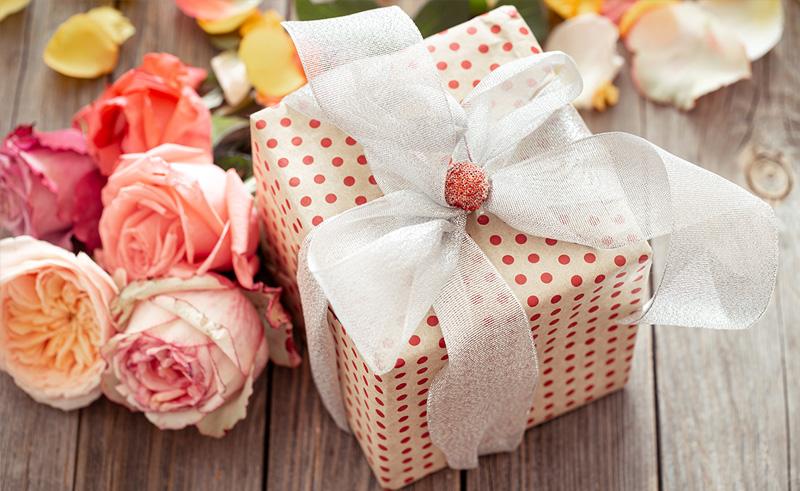 Người yêu đang mở một hộp quà nhỏ có ruy băng, khuôn mặt ngạc nhiên và hạnh phúc trong ngày 8/3, bối cảnh lãng mạn với hoa và ánh nến